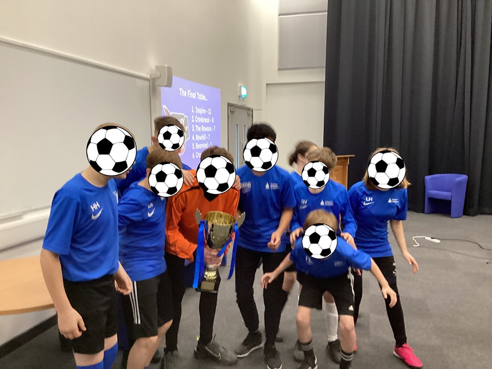 A group of students are shown posing for the camera together for a photo holding the Football Tournament trophy they have won.