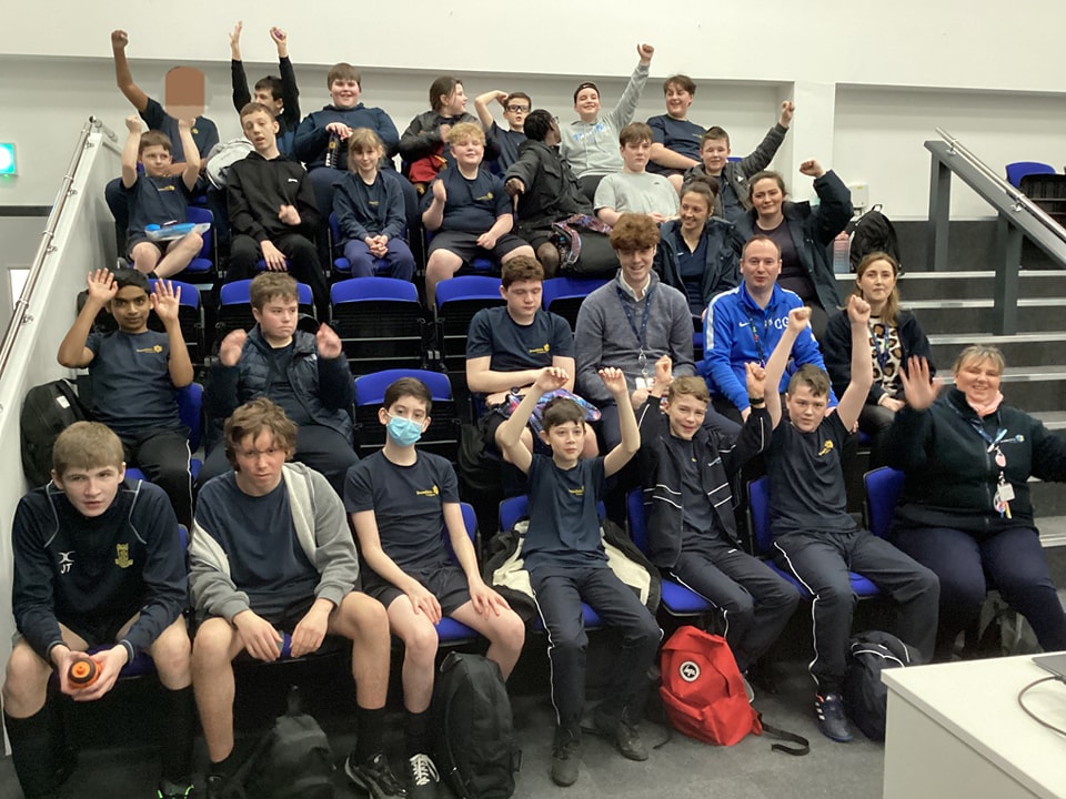 A large group of Leigh Academy Snowfields students can be seen sat down at in the tiered seating in the Sports Hall, ready to watch an academy Football match.