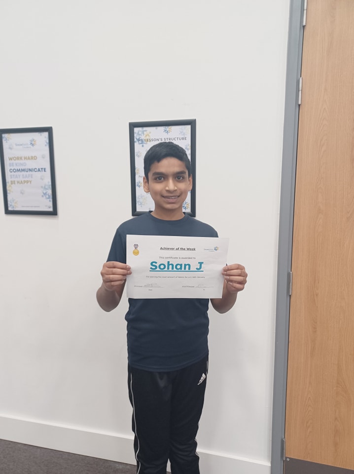 A young boy is seen smiling for the camera and holding up a certificate he has won.