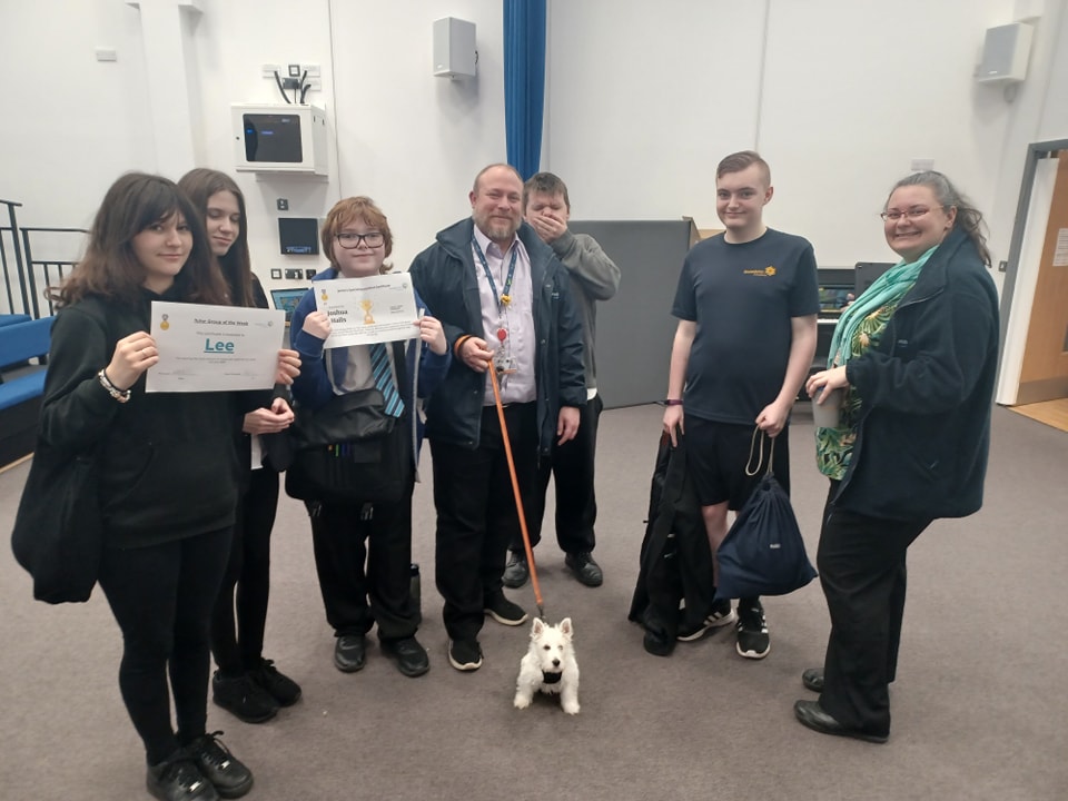 A group of staff and students are pictured smiling together for the camera, whilst holding certificates they have won for activities they have participated in.