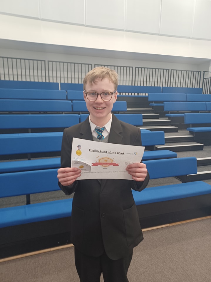 A student can be seen smiling for the camera, whilst holding up a certificate he has won from participating in an activity.