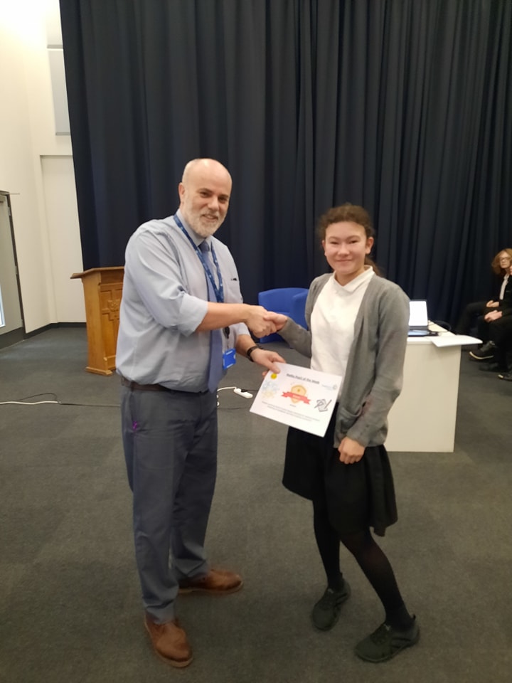 A student is seen posing for a photo for the camera, whilst collecting a certificate she has won from a male member of staff.