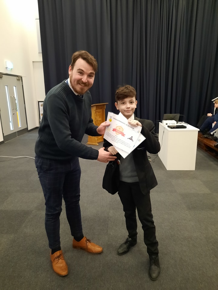 A teenage boy is shown being presented with a certificate he has won by a member of staff.