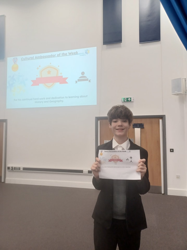 A student can be seen smiling for the camera, whilst holding up a certificate he has won from participating in an activity.