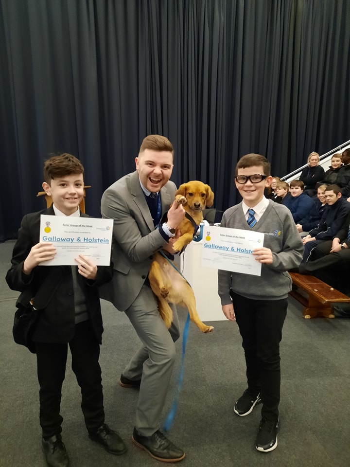 Two Leigh Academy Snowfields students are seen posing for a photo alongside a member of staff carrying a pet Dog in his hands.