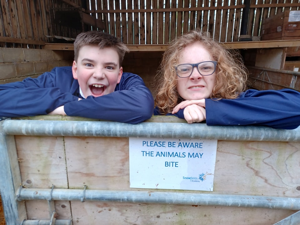 Two Leigh Academy Snowfields students, a boy and a girl, are seen peering out over from behind a barn gate and smiling for the camera.