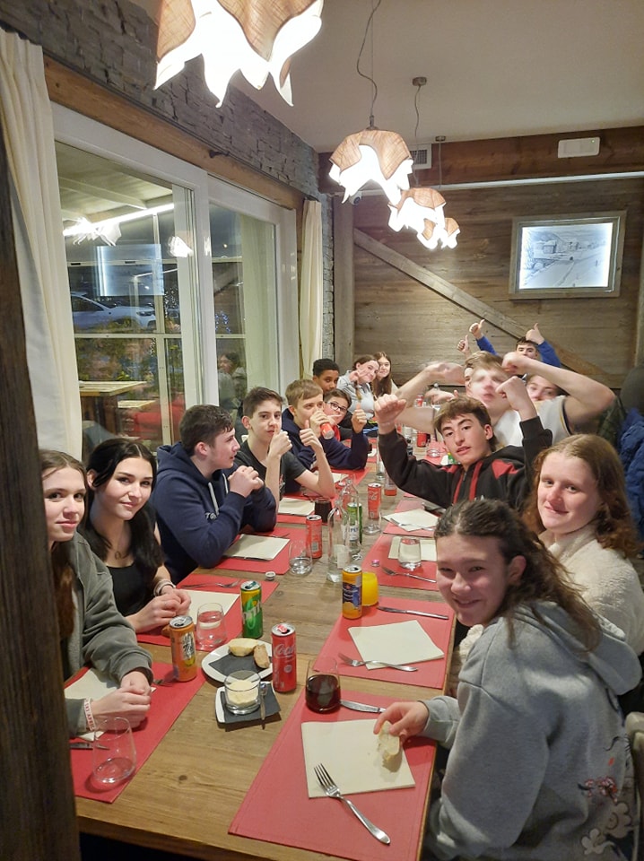 A large group of students from Leigh Academy Snowfields can be seen sat around a long table, as they prepare to have dinner during a skiing trip abroad.