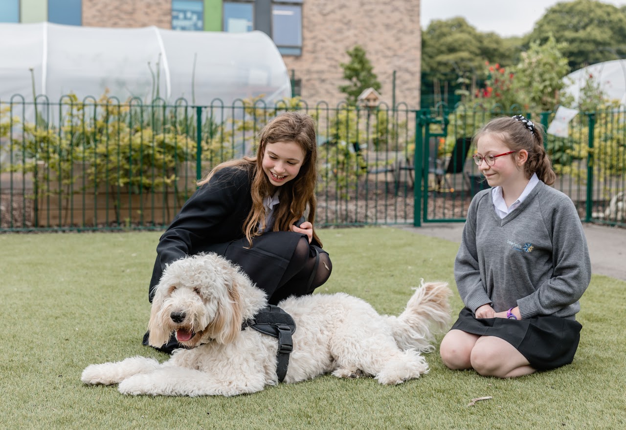 2 students sat on a field with a dog laying down